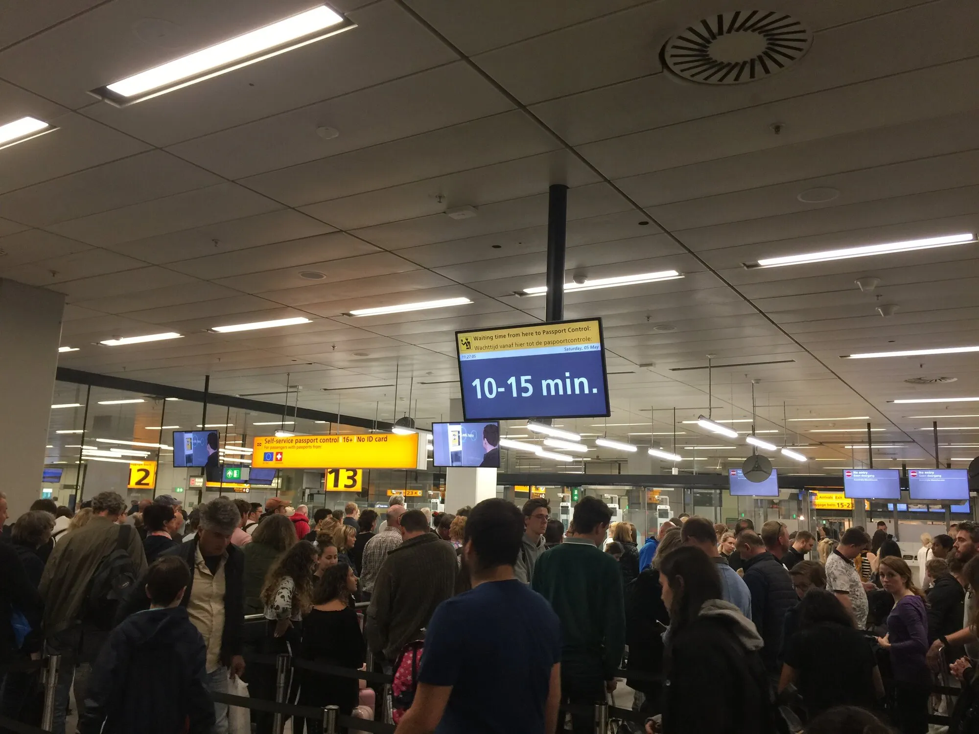 People staying in line for passport control, monitor above shows approximate wait time: 10-15 minutes