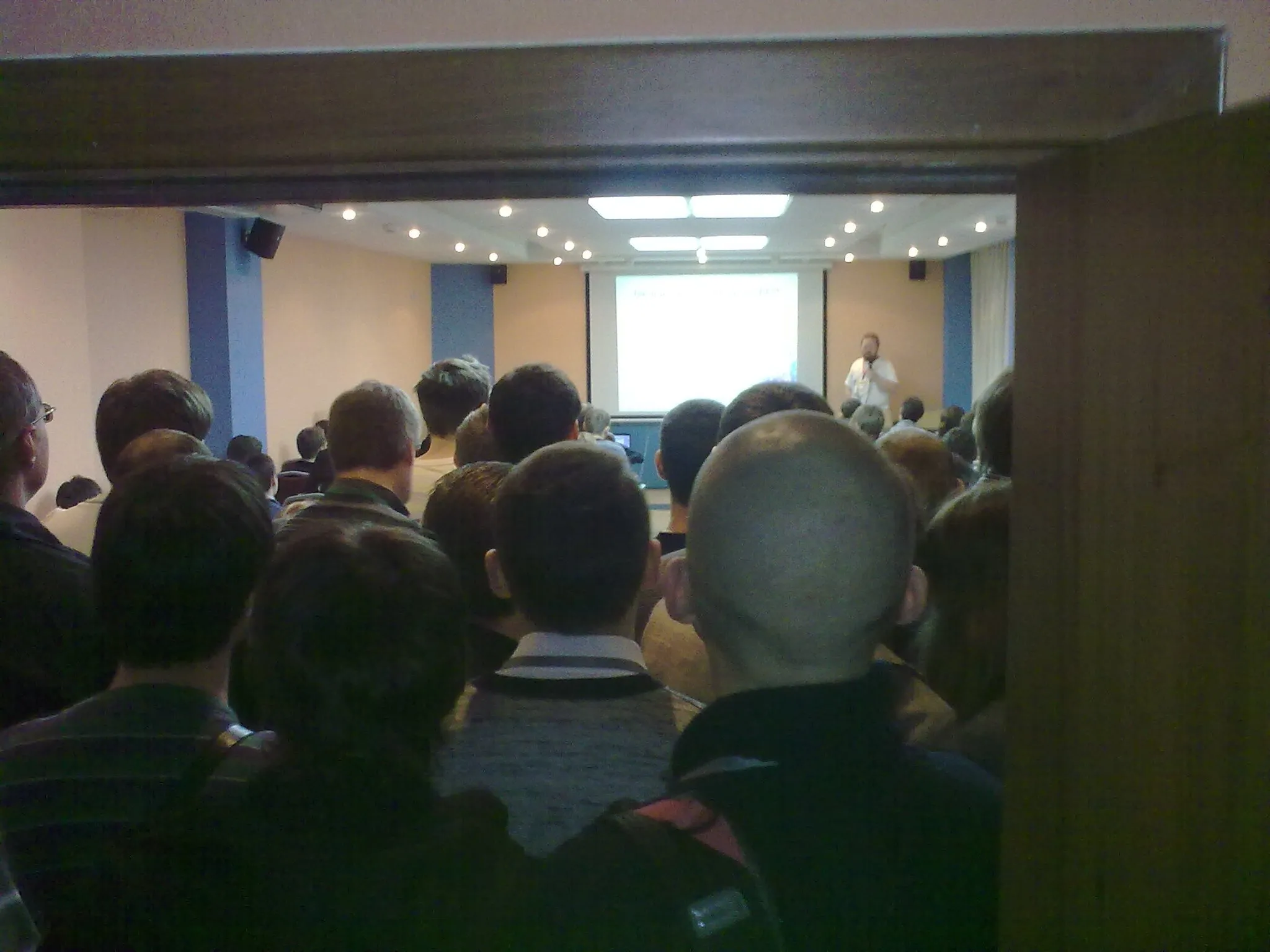 A lot of people watching a talk while stying at the entrance because there are not enough space in the room
