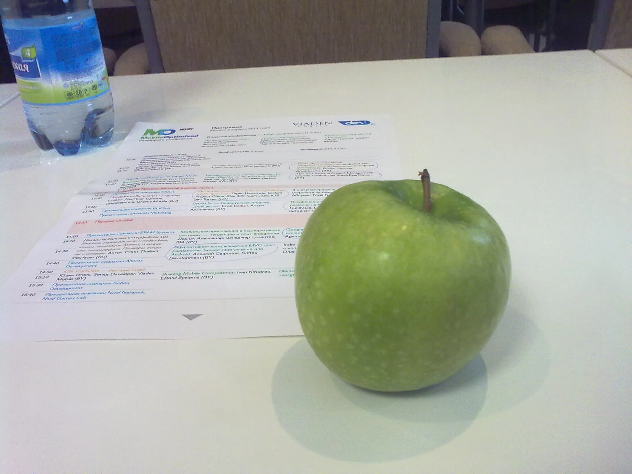Green apple and program of the conference are on the white table